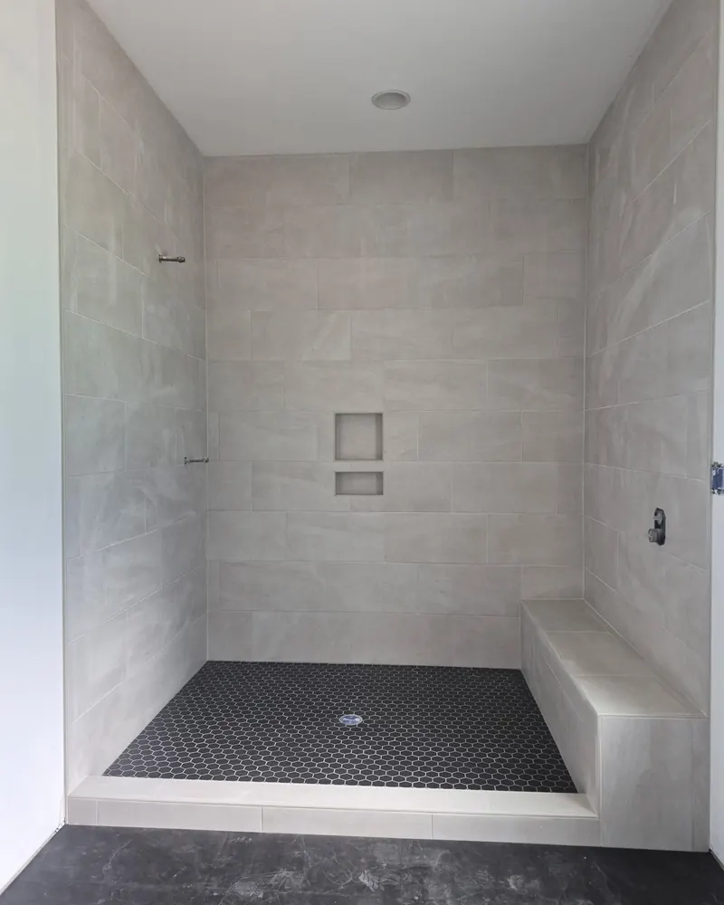 Light tile shower with a bench and a black hex floor