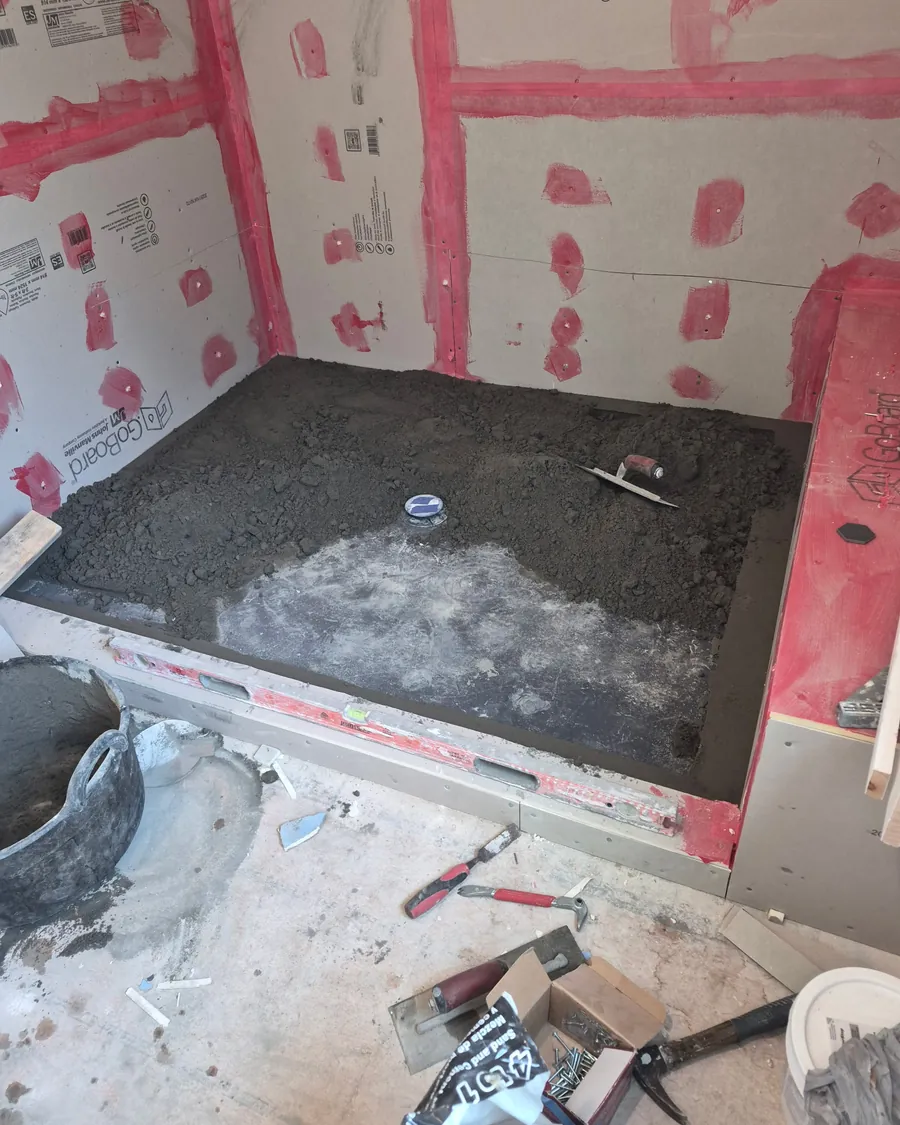 Shower pan mortar bed sloped to the drain, surrounded by waterproofed board with sealed seams