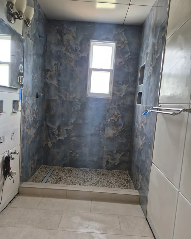 Blue marble-look shower with a pebble floor and glass enclosure